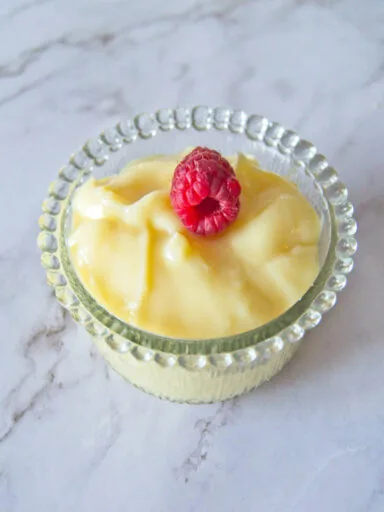 vanilla pudding served in a glass bowl and topped with raspberry