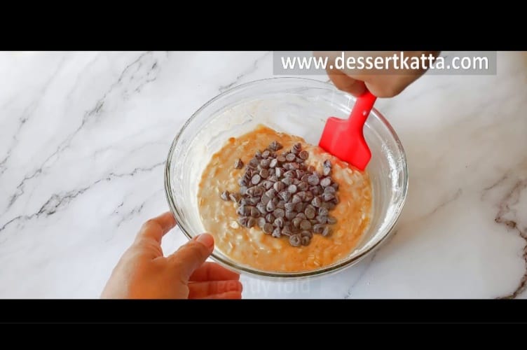 chocolate chips are added to muffin batter and mixing with red spatula