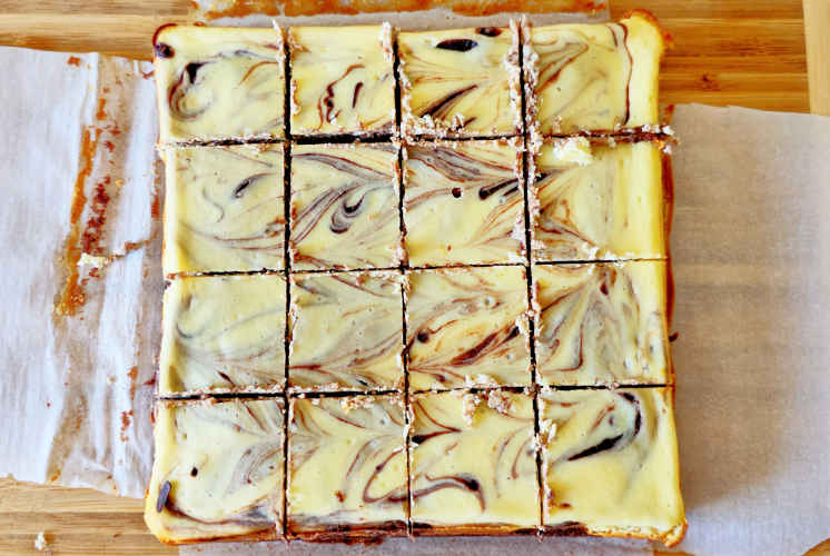 top shot of Chocolate cheesecake brownies cut into 16 pieces placed on parchment paper on wooden board