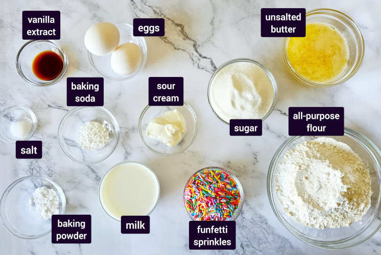 ingredients for funfetti muffins are placed on marble background in small bowls
