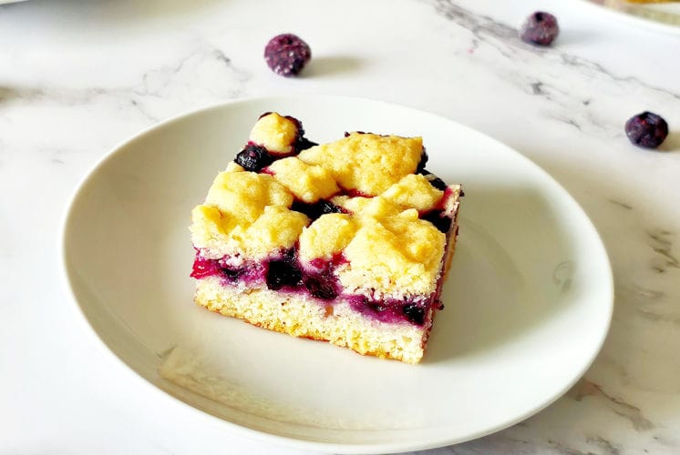 single lemon blueberry bar placed in a white plate kept on white background with few blueberries in the background