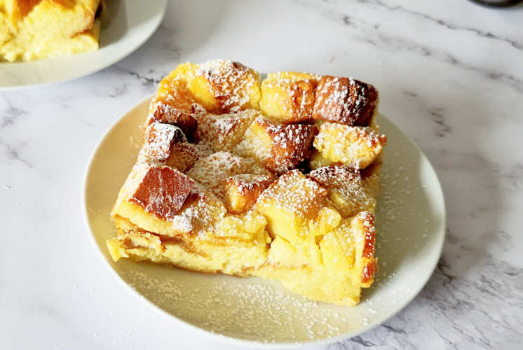 single serving of vanilla bread pudding is served on a white plate and dusted with powdered sugar