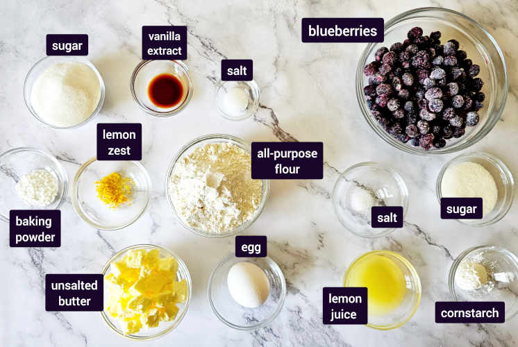 ingredients for lemon blueberry bars are placed on marble background in small bowls