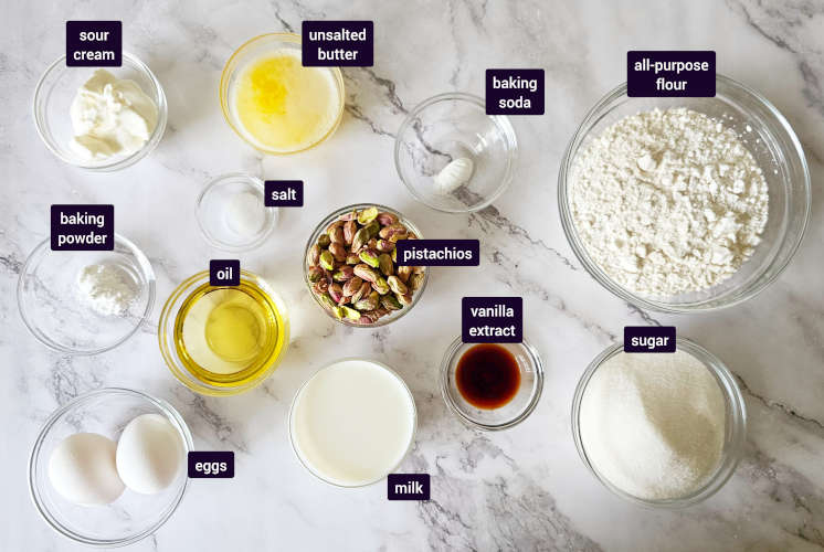 ingredients for pistachio muffins are placed on marble background in small bowls