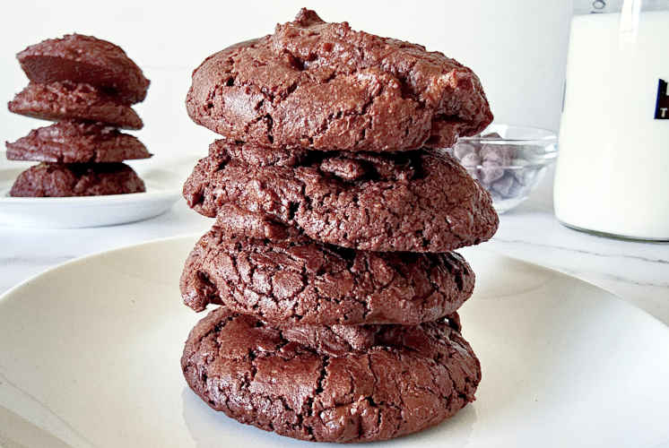 front shot of chocolate brownies cookies with some cookies, chocolate chips and milk bottle in the background